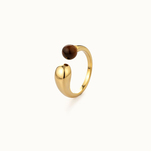 A gold-toned open ring with a smooth, rounded polished tiger eye natural stone bead on the top, set against a clean off-white background.