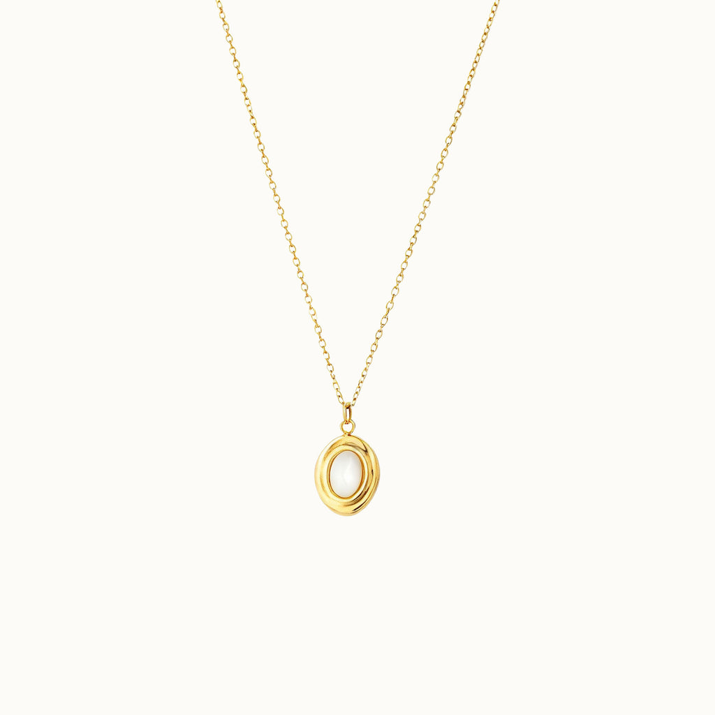 A delicate gold chain necklace with a small oval mother of pearl pendant featuring a polished gold outer ring and a smooth white center, displayed against a solid off-white background.