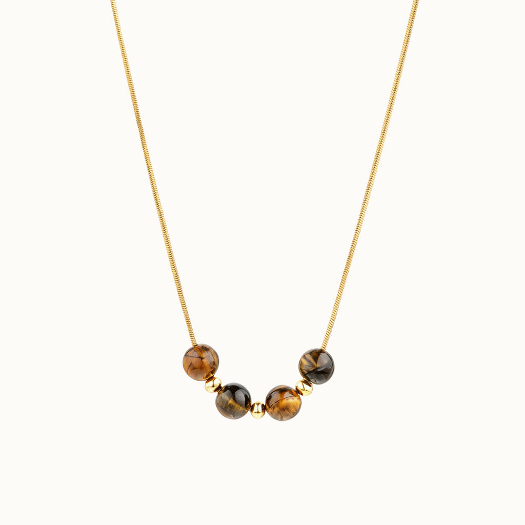 A delicate gold chain necklace featuring five polished brown and black tiger's eye beads spaced along the front, displayed against a clean off-white background.