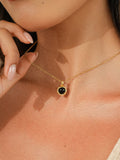 A close-up lifestyle shot of a model wearing a delicate gold chain necklace with a small circular black gemstone pendant.